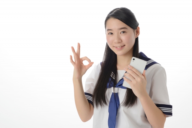 スマホを持ってOKサインを出す女子中学生