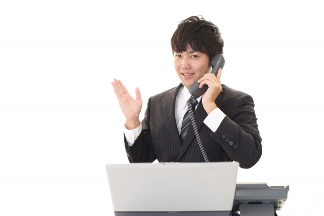 ノートパソコンを見ながら電話対応をしている男性
