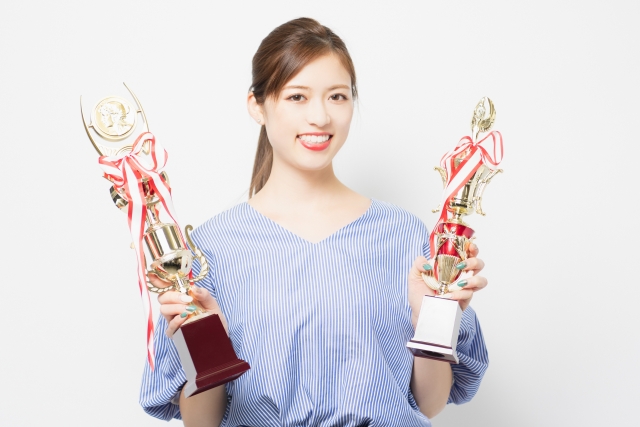 若い女性が笑顔で両手にトロフィーを持っている