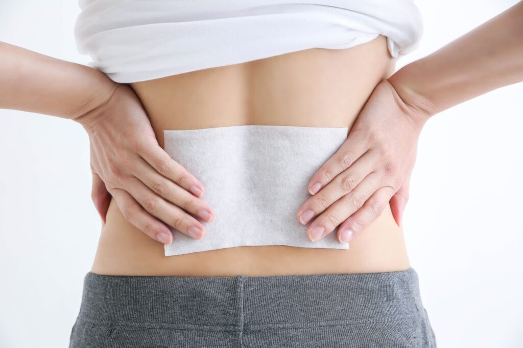 腰に湿布を貼って両手で押さえている女性