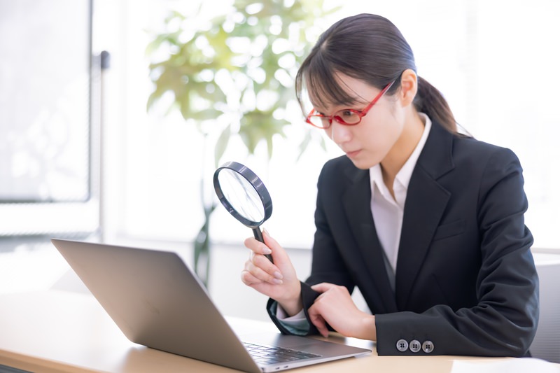 拡大レンズを持ってノートパソコンで調べものをしている女性