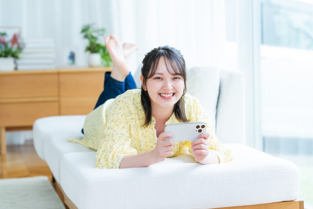 マットレスに横たわるスマホを見ている女性